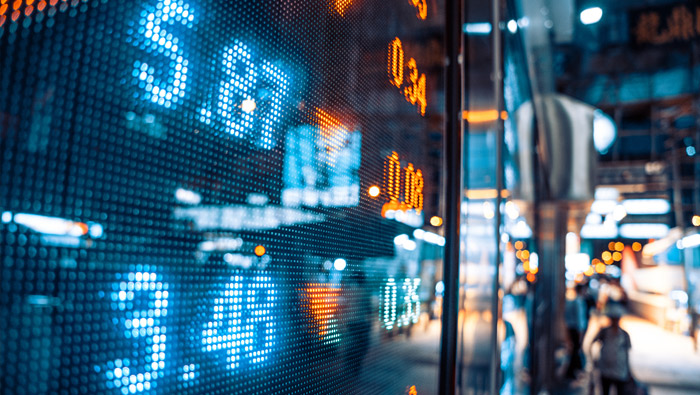 Financial numbers flash on an outside display with pedestrians and traffic going past.