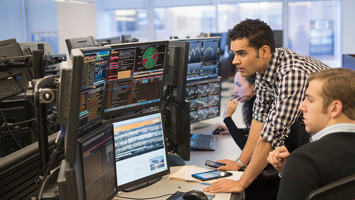 Two IT experts look at a set of monitors displaying data