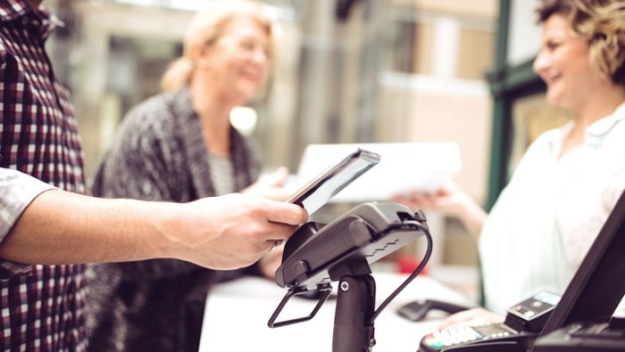 A man pays cashless by holding his phone over a scanner.