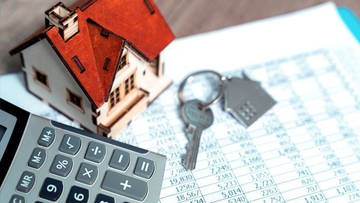 A calculator, model of a house and keys are lying on a spreadsheet.