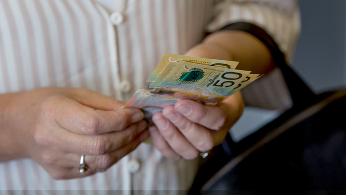 The hands of an older woman holding a few 50 dollar notes.