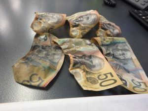 Six $50 banknotes on a black table in various shrunken and warped shapes.